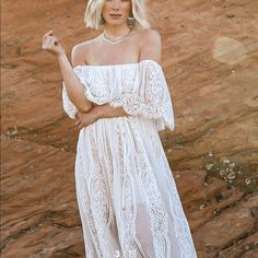 a woman wearing a white dress standing in front of a rock formation with her arms crossed