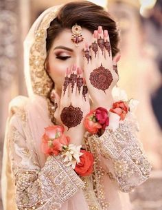 a woman with her hands painted in henna and flowers on her face, holding her hands up to her face