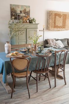 a dining room table set for four with blue linens and wicker chairs in front of it