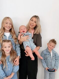 a group of people standing next to each other in front of a white wall holding a baby