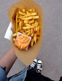 a person holding a paper plate with french fries and ketchup in it on the ground