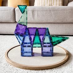 a purple and green glass sculpture sitting on top of a wooden stand in front of a couch