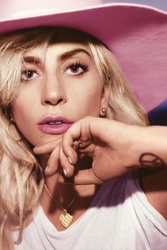 a woman with long blonde hair wearing a white shirt and pink hat is looking at the camera