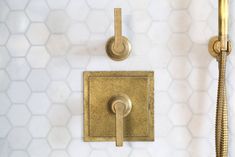 a gold faucet mounted to the side of a white tiled wall next to a shower head