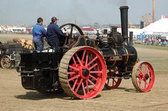 two men standing on the back of an old fashioned steam powered tractor in a field