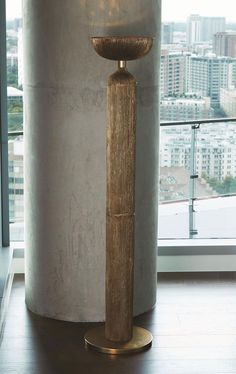 a tall wooden candle holder sitting in front of a window next to a large wall