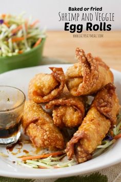 fried shrimp and vegetable egg rolls on a plate next to a bowl of coleslaw