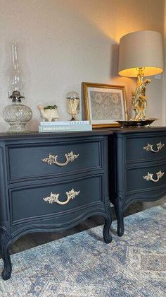 two black dressers with gold handles in a living room next to a lamp and pictures on the wall