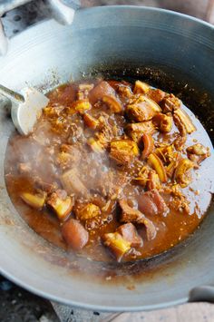 a pot filled with meat and vegetables on top of a stove burner next to a wooden spoon