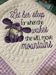 a purple and white quilted pillow with a teddy bear on it that says let her sleep for when she wakes, she will move mountains