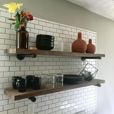 two shelves with vases, plates and cups on them in front of a white brick wall