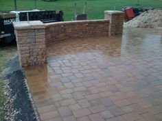 a brick patio with an outdoor fireplace and grill in the back ground, surrounded by grass