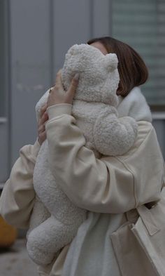 a woman holding a large white teddy bear in her arms and covering her face with both hands