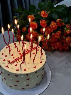 a birthday cake with candles that spell out the word happy on it and roses in the background