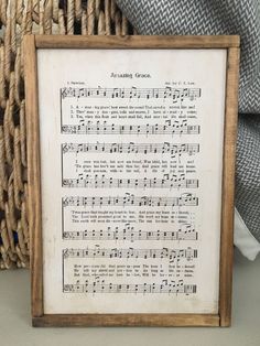 an old sheet music is displayed in a wooden frame on a wicker basket next to a pillow