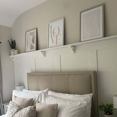 a bed with white linens and pillows in a small room next to some pictures on the wall