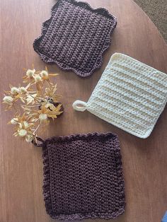 three crocheted potholders sitting on top of a table next to a vase with flowers