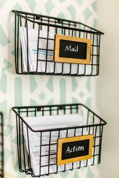 two black wire baskets with labels on them hanging from the side of a white wall