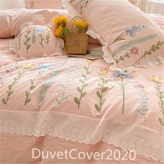 a bed with pink comforter and flowers on the pillowcase, next to a basket full of sunflowers