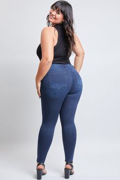 a woman in high waist jeans and heels is looking back at the camera, with her hands on her hips