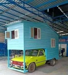 a small blue house with a yellow car in the garage next to it on wheels