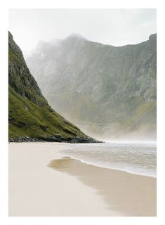 an empty beach with mountains in the background and fog on the water's surface