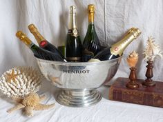 a silver bowl filled with champagne bottles next to two sea shells and a starfish