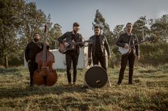 three men are standing in the grass with their instruments