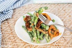 a white plate topped with green beans and fried food next to a blue striped napkin