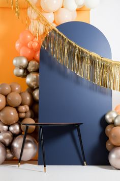 an empty chair in front of balloons and streamers on the wall with a gold fringe