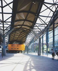 an empty train station with the sun shining on it's roof and people walking around