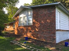 a small brick house sitting in the middle of a yard next to trees and grass