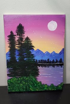 a painting of a lake and trees with the moon in the sky above it on a table