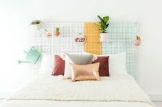 a white bed topped with lots of pillows next to a wall mounted potted plant