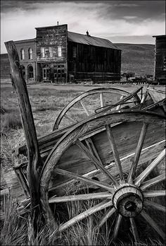 an old wooden wagon sitting in front of a building with two barns on the other side