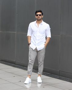 a man in white shirt and grey pants standing on sidewalk with his hands in his pockets