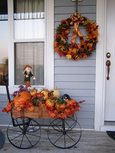 a wheelbarrow with pumpkins and gourds on the front porch