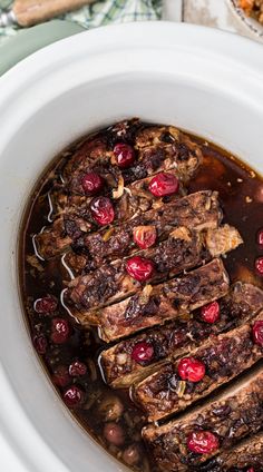 meat and cranberry sauce in a white slow cooker with spoons on the side