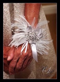 an older woman's hands are adorned with white feathers and brooches as she holds her husband's hand