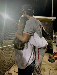 a man and woman standing next to each other in front of a baseball field at night