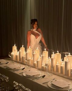 a woman standing in front of a long table with many lit candles on top of it