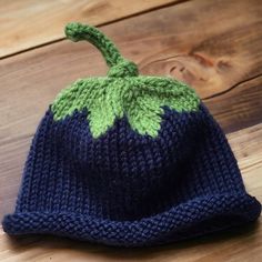 a knitted hat with a green leaf on the top sits on a wooden surface