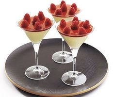 three martini glasses filled with strawberries on top of a black serving platter next to each other