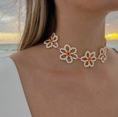 a woman wearing an orange and white beaded flower necklace on the beach at sunset