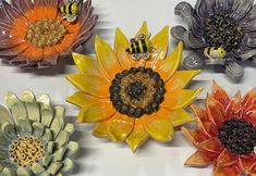 five ceramic sunflowers with bees on them are shown in different colors and sizes