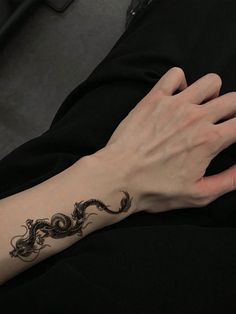 a woman's arm with a black dragon tattoo on her left wrist and right hand