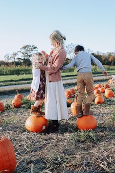 a woman and two children standing in front of pumpkins on the ground with their arms around each other