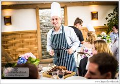 a chef standing in front of a table filled with food and people sitting around it