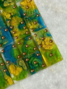 several square tiles with gold and green designs on them sitting on a white table top