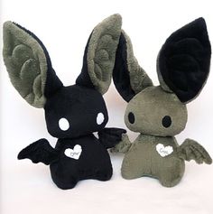 two small stuffed animals sitting next to each other on a white surface with one black and the other green